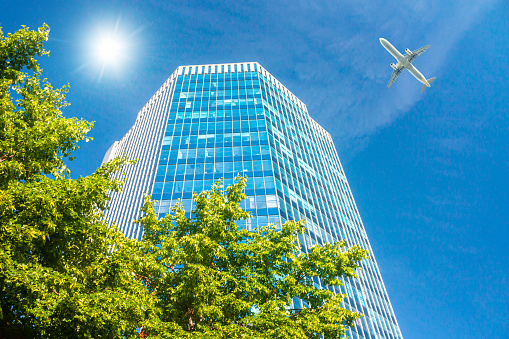 A modern office skyscraper and white passenger airplane flying over this building