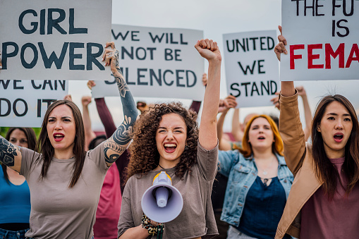 Group of young women protesting for equality and women's rights. Holding hand-made signs on cardboard and marching together in the city streets