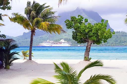 Moorea, French Polynesia - 2001: A  photograph of the beach on Motu island off the coast of Bora Bora with island mountain and cruise ship in background through palm trees as shot on the rare Canon EOS 1N - Kodak DCS 520, one of the first professional digital cameras.