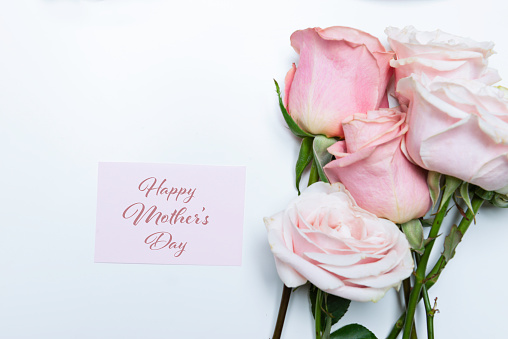 Pink roses and pink Happy Mother’s Day  greeting card on white table.