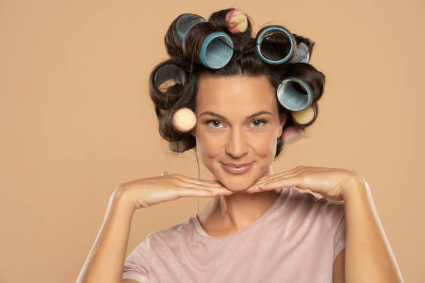 Beautiful woman with hair curlers posing on a beige background stock photo