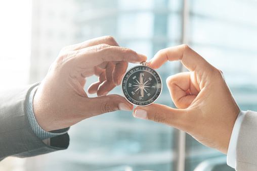 Hands of two business persons are holding a compass in front of a skyscraper.