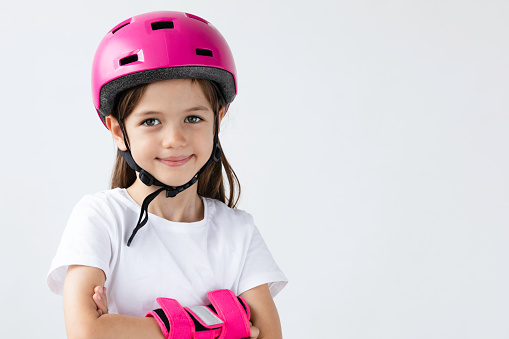 Little girl is wearing a pink helmet and wrist protection and is looking at camera on pure white background. She is about to learn skating