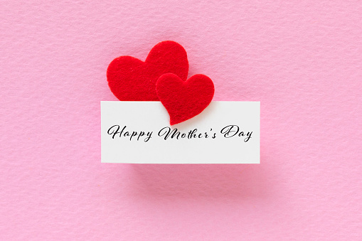 Red heart shapes attached to a white card with Happy Mother’s day text on pink background.