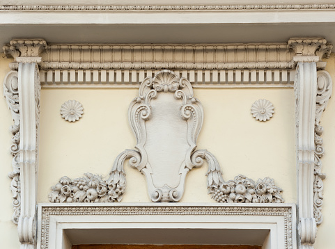 A part of the facade of an old building with beautiful stucco decoration and bas-relief of a blank family emblem