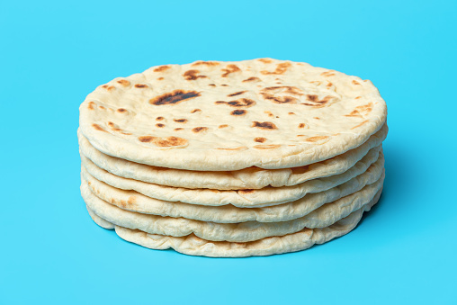 Stack of indian flatbreads minimalist on a blue table. Homemade naan bread, asian traditional food.