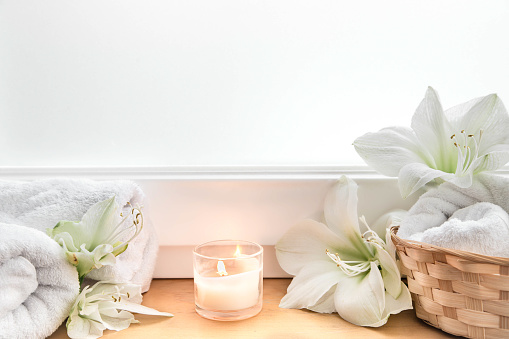 Home spa composition with lily flowers, candle and towels in a basket, copy space.
