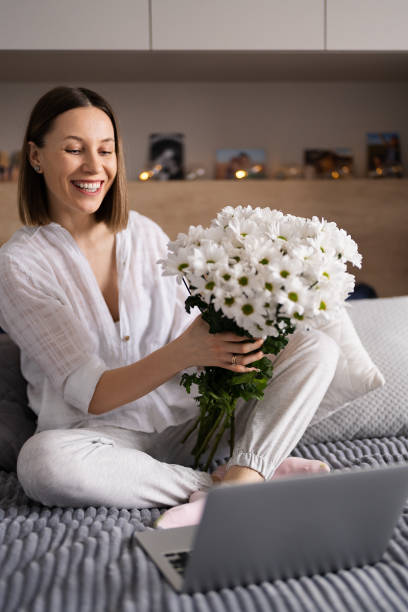 istock Woman communicating using a laptop while stating on bet with a bunch of white flowers 1456886045