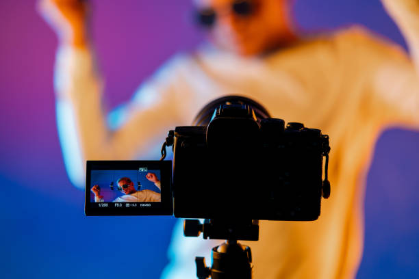istock Backstage how operator working with professional camera. Videographer shoots music clip with actor or singer celebrity woman in colorful studio with neon color light. 1456886256