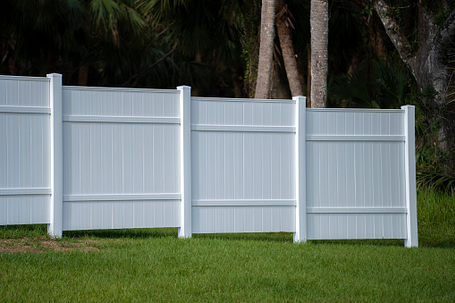 White vinyl picket fence on green lawn surrounding property grounds for backyard protection and privacy.
