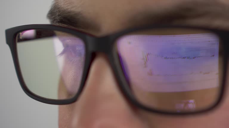 Reflection of the stock chart in glasses from the investor. A young man trades on the stock exchange and closely follows the chart. Glasses close-up. 4k