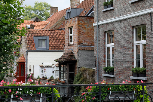 Bruges, Belgium - September 9, 2022: There is a view of brick houses. On the railing of a small bridge, flowers grow in pots and leaves of trees are also seen
