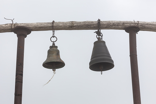 Simple wooden belfry with two hanging bells against foggy background next to Saint Giorgi Church in Khvamli Mountain range in Georgia.