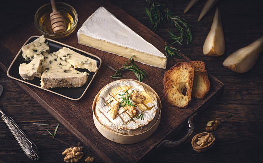 Cheeses of France: Camembert, Brie and Roquefort on a rustic antique background served with rosemary, nuts, pears. Cheese board. French classic cheeses