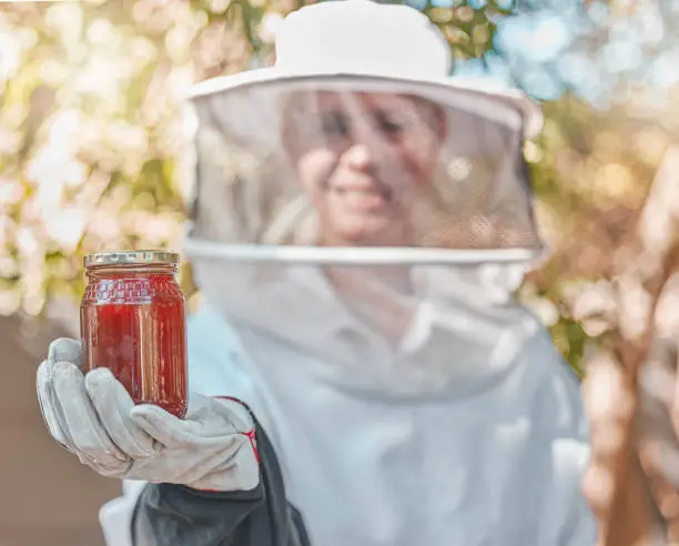 Hand, honey and jar with a woman beekeeper working in the countryside in the production of a natural product. Farm, agriculture and sustainability with a female farmer holding a honeyjar outdoor