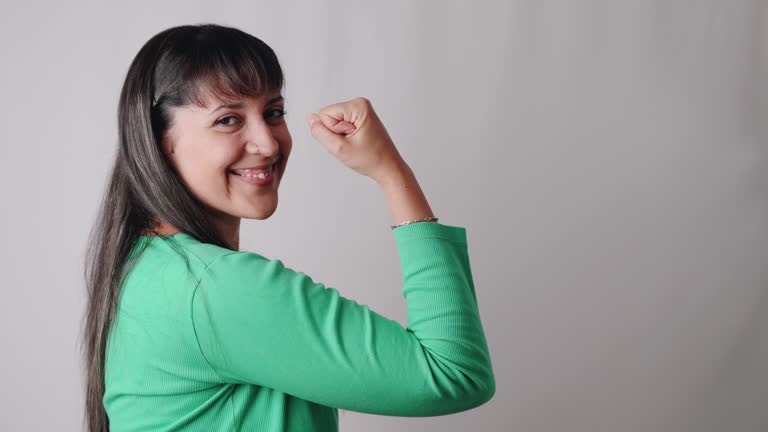 Latin real woman showing her biceps on feminism and empowerment sign while looking at camera. Real people concept