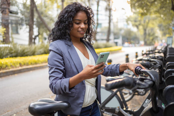 Young woman using mobile phone to rent a bike Businesswoman renting the bike from bicycle sharing system rent a bike stock pictures, royalty-free photos & images