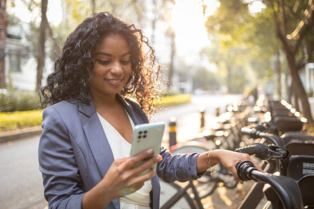 mujer joven usa el teléfono móvil para alquilar una bicicleta - bikeshare fotografías e imágenes de stock