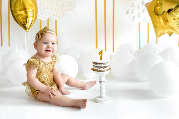 istock A cute one-year-old girl in a shiny bodysuit with a cake on her first birthday 1456906708