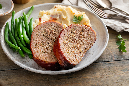 Meatloaf portion on a plate served with mashed potatoes and green beans