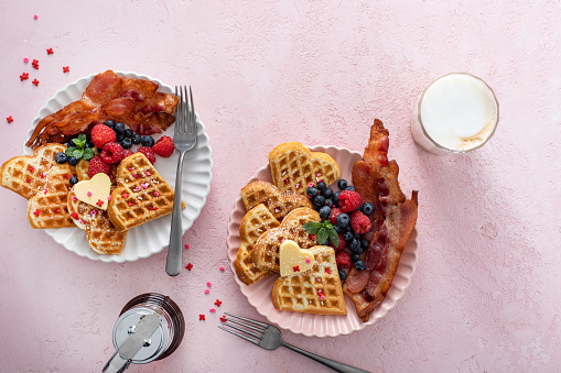 Valentine day breakfast for two with waffles heart shaped on pink, top view