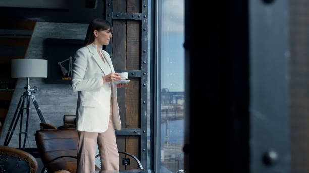 Thinking woman drinking coffee at panorama window. Lady resting with beverage