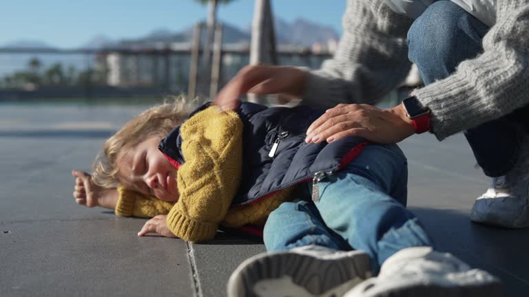 2 year old having a tantrum on the ground outdoor while a woman comforts him.