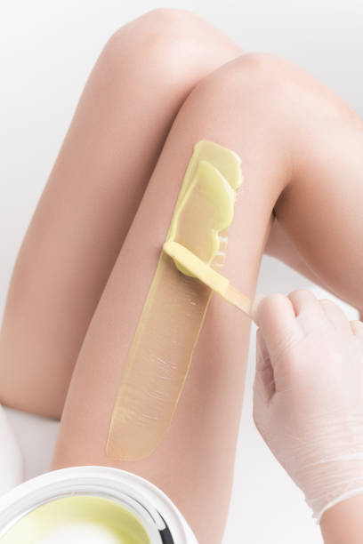 Applying hot wax on slim woman leg using spatula. Professional depilation, waxing in beauty salon stock photo