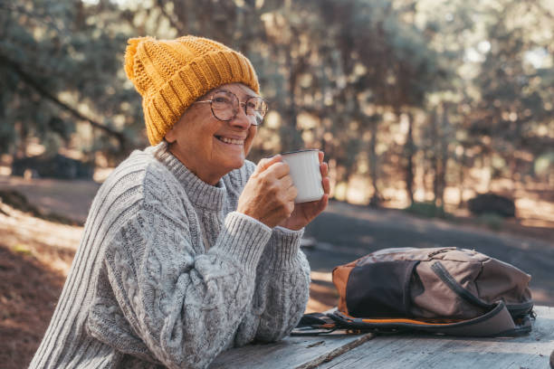 head shot portrait close up of middle age woman relaxing drinking coffee or tea sitting at table in the forest of mountain in the middle of nature. autumn season enjoying concept lifestyle. - senior adult cheerful adventure discovery imagens e fotografias de stock