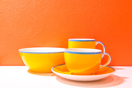 Plate  and cups with orange wall and white floor, Thailand.