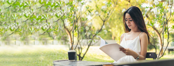 banner frau hält buch lesemagazin im grünen park naturgarten. junge frau entspannung lesen offenes buch selbststudium. glück universitätsfrauen lächeln. frauen sitzen im grünen park mit kopierraum - nature writing women ideas stock-fotos und bilder