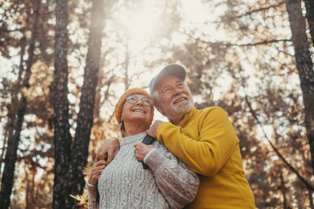 portret z bliska wesołych ludzi w średnim wieku, uśmiechniętych i patrzących na drzewa otaczającego ich lasu. aktywna para starszych seniorów wędrujących i spacerujących razem po górach, dobrze się bawiących. - senior adult mountain hiking recreational pursuit zdjęcia i obrazy z banku zdjęć