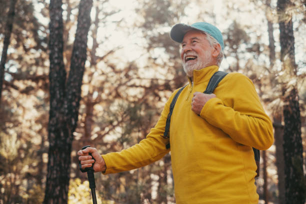 primo piano del ritratto di mezza età dell'uomo caucasico che cammina e si gode la natura in mezzo agli alberi nella foresta. vecchio maschio maturo che indossa gli occhiali che cammina e scopre. - hiking senior adult exercising outdoors foto e immagini stock