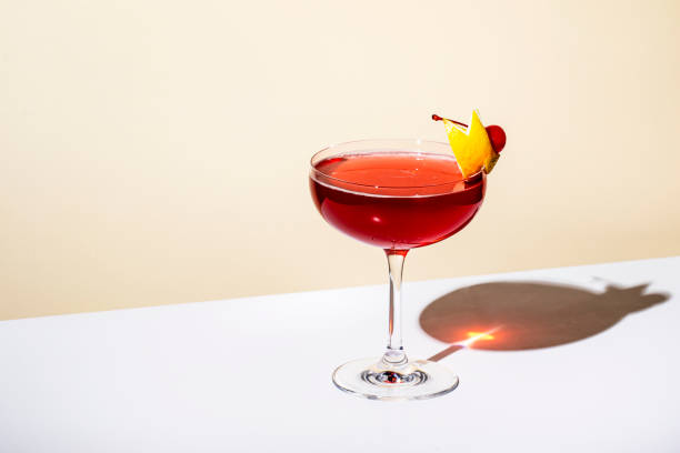 New Yorker cocktail with whiskey, grenadine, bitters, lemon juice and ice, garnished with lemon zest and cherries in glass. Beige background, hard light stock photo