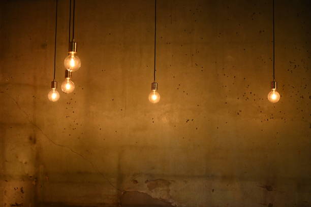 istock Orange hanging light bulb against old cement wall 1456948106