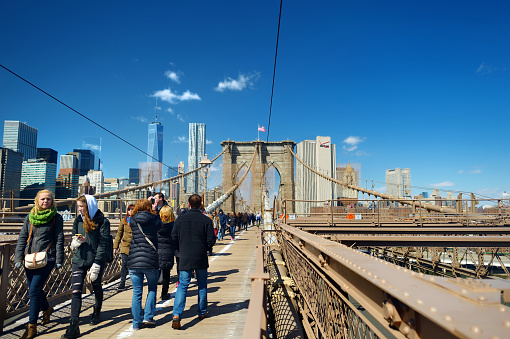 New York - March 22, 2015: People walking on Brooklyn Bridge. Tourists enjoying view of Brooklyn Bridge gate and Manhattan skyline on the background.