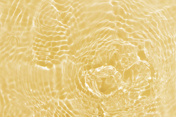 ぼかした透明な金色の透明な穏やかな水面テクスチャーと水しぶきと泡の焦点をぼかします。トレンディな抽象的自然の背景。コースティクスと日光の下で水の波。輝く黄色い水