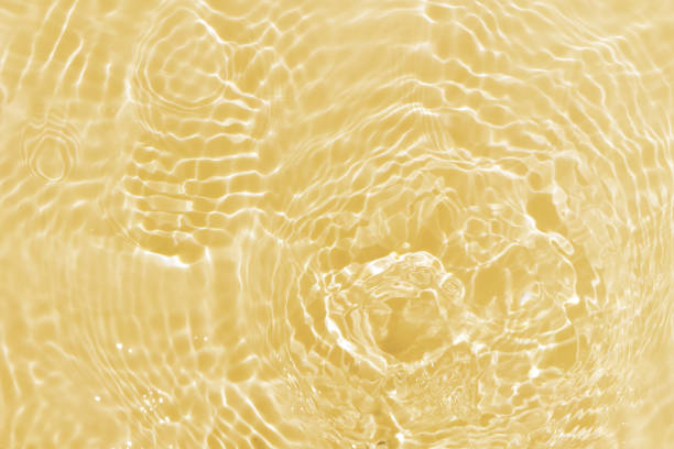 Defocus blurred transparent gold colored clear calm water surface texture with splashes and bubbles. Trendy abstract nature background. Water waves in sunlight with caustics. Yellow water shinning
