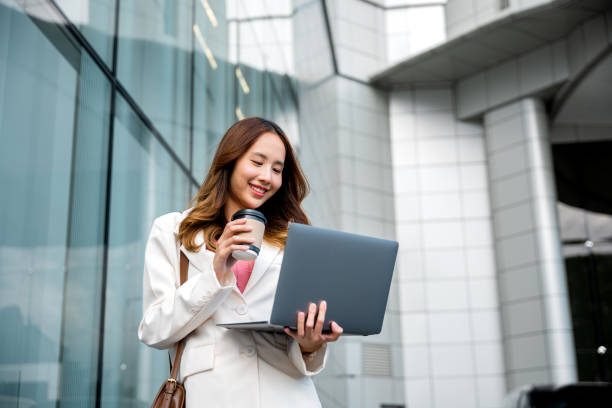 istock Confident businesswoman using computer laptop standing while drinking a cup of coffee 1456958701
