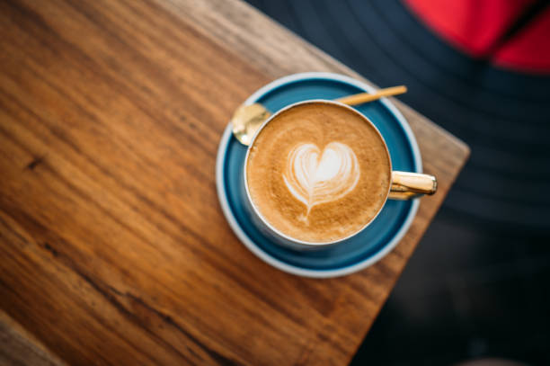 nahaufnahme heiße cappuccino weiße kaffeetasse mit herzform latte kunst auf dunkelbraunen alten holztisch im café - nobody drink hot drink coffee stock-fotos und bilder