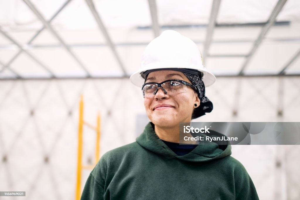 Woman Construction Worker On Job Site A multiethnic woman wears a hardhat and safety glasses while working on an interior project. Labor Union Stock Photo