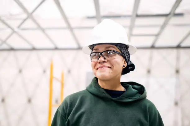 A multiethnic woman wears a hardhat and safety glasses while working on an interior project.