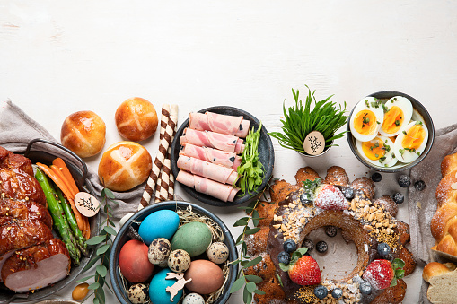 Traditional Easter dinner or  brunch with ham, colored eggs, hot cross buns, cake and vegetables. Easter meal dishes with holday decorations. Top view, copy space