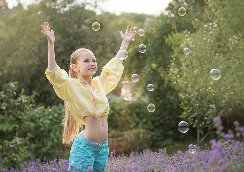 Beautiful little girl catches soap bubbles in a field with lavender