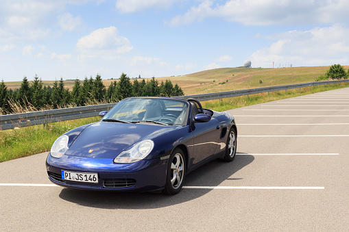 Gersfeld, Germany - July 23, 2021: Blue roadster Porsche Boxster 986 with Wasserkuppe panorama and radar dome in Rhön Mountains. The car is a mid-engine two-seater sports car manufactured by Porsche.