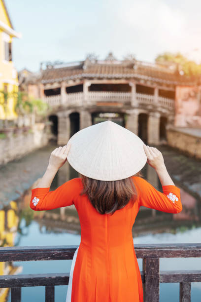 Woman traveler wearing Ao Dai Vietnamese dress sightseeing at Japanese covered bridge in Hoi An town, Vietnam. landmark and popular for tourist attractions. Vietnam and Southeast Asia travel concept Woman traveler wearing Ao Dai Vietnamese dress sightseeing at Japanese covered bridge in Hoi An town, Vietnam. landmark and popular for tourist attractions. Vietnam and Southeast Asia travel concept exhibition place toronto stock pictures, royalty-free photos & images