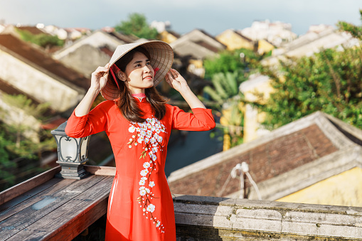 happy woman wearing Ao Dai Vietnamese dress, traveler sightseeing view at rooftop at Hoi An ancient town in Vietnam. landmark and popular for tourist attractions. Vietnam and Southeast travel concept