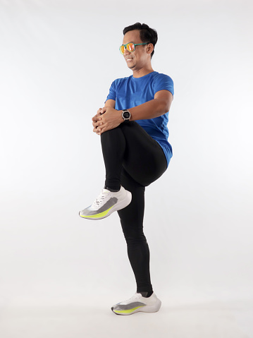 Asian male runner warming up prepararing his body before running workout. stretch his leg muscle, studio full length portrait against white background