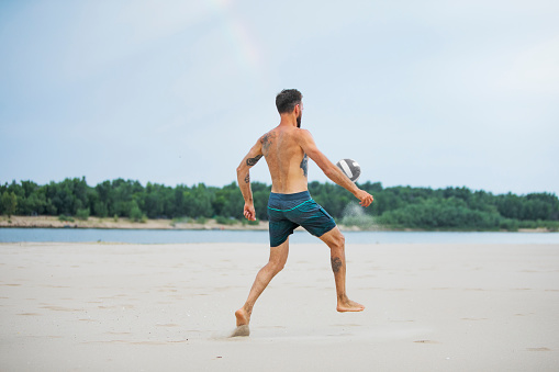 Young adult man playing football at the beach
