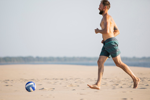 Young adult man playing football at the beach